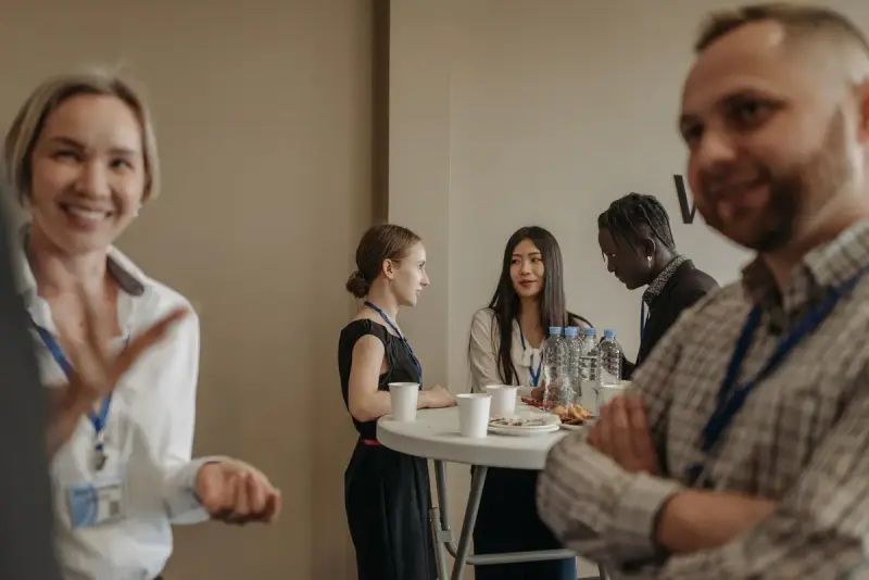 Professionals with lanyards talking and laughing at a standing table during a conference break