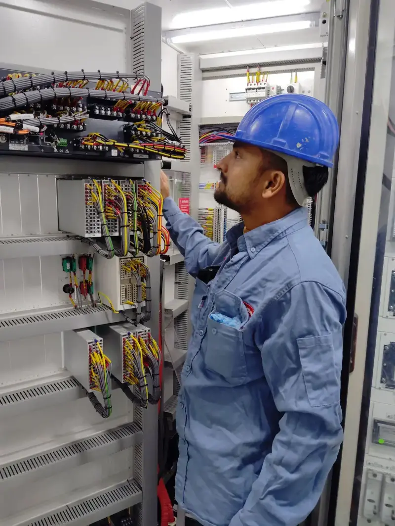 Technician in a blue hard hat checking wiring inside an open control cabinet