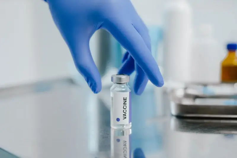 Blue-gloved hand reaching for a glass vial on a steel work surface
