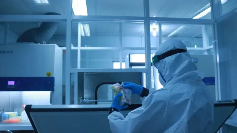 Technician in a full protective suit and face shield working at an enclosed lab station