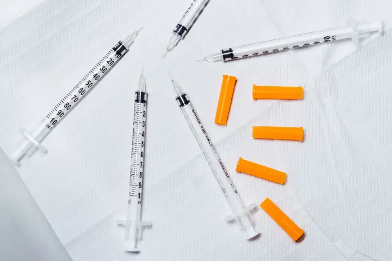 Disposable syringes with orange needle caps laid out on a white surface