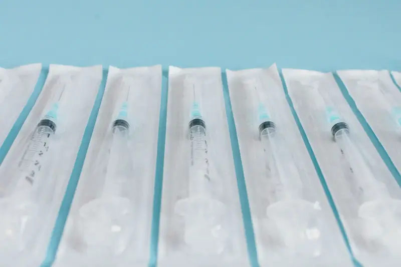 Row of sterile syringes sealed in individual blister packaging on light blue