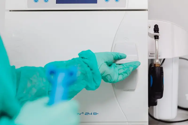 Gloved hand in a sterile gown closing the door of a benchtop steam sterilizer