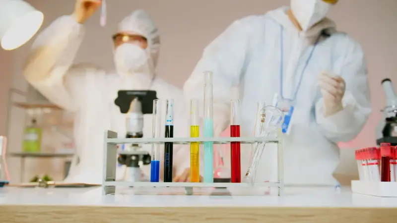 Two scientists in protective suits and masks working with test tubes and microscopes