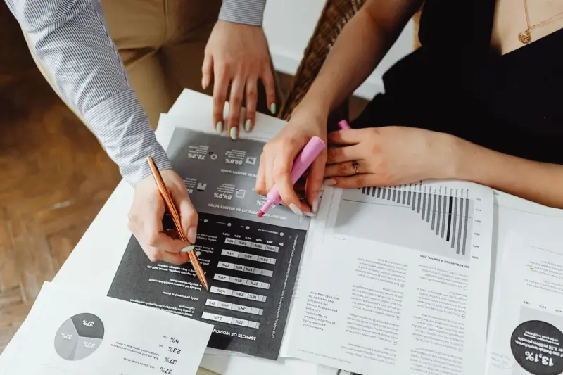 Hands marking printed charts and graphs with pens and highlighters
