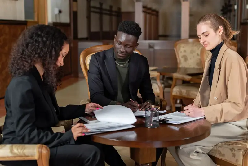 Three colleagues reviewing and signing documents around a table