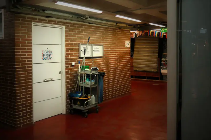 Cleaning cart with mop and bucket parked by a door in a long brick-walled service hallway
