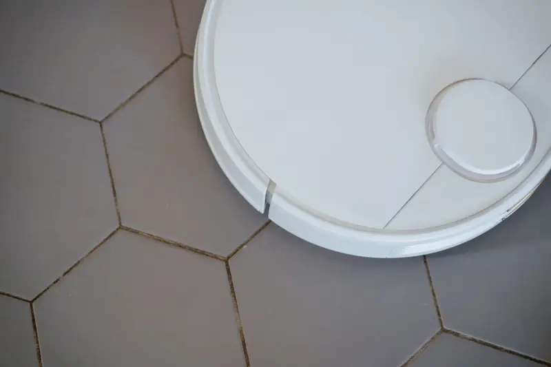 White robotic vacuum seen from above on gray hexagonal floor tiles