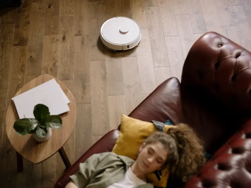 Robot vacuum crossing a hardwood floor beside a leather sofa and small side table