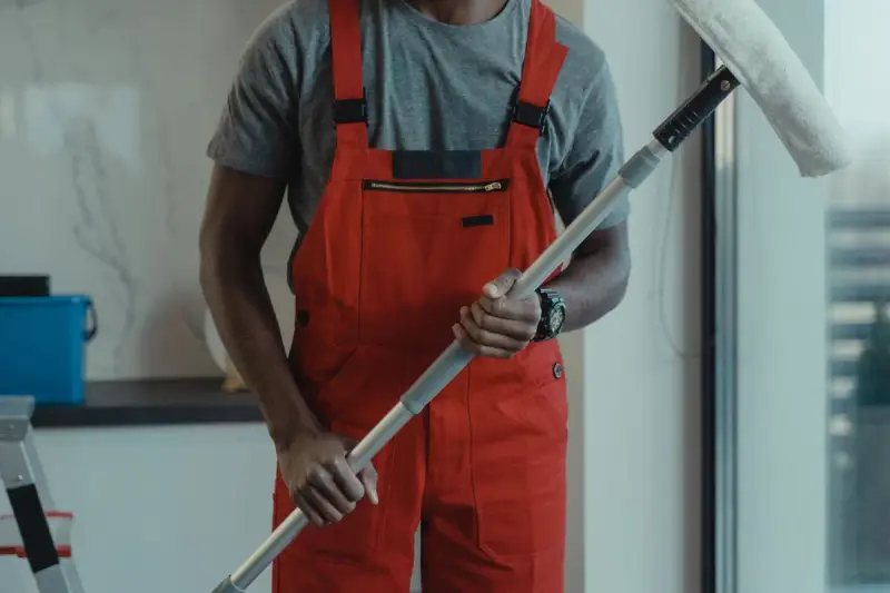 Professional cleaner in red overalls holding a long-handled window mop