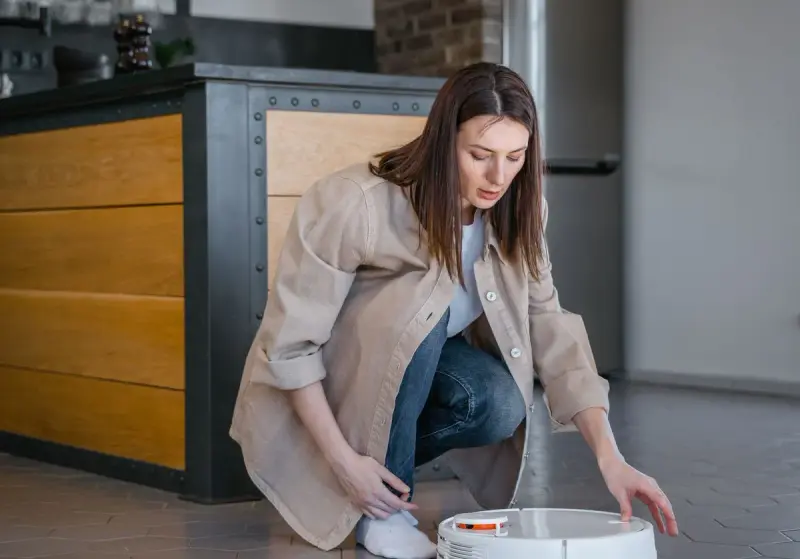 Woman kneeling to set up a white robot vacuum on a kitchen floor