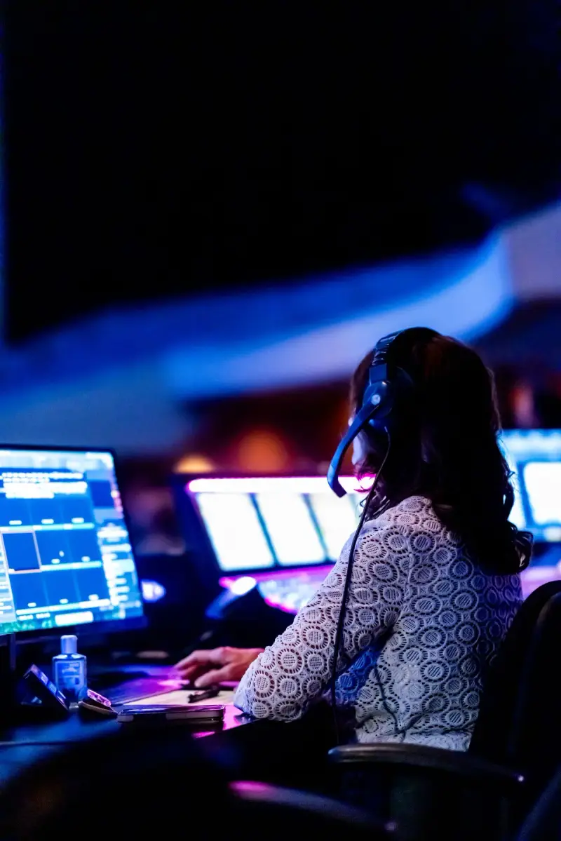 Woman wearing a headset at a control room desk with several computer screens