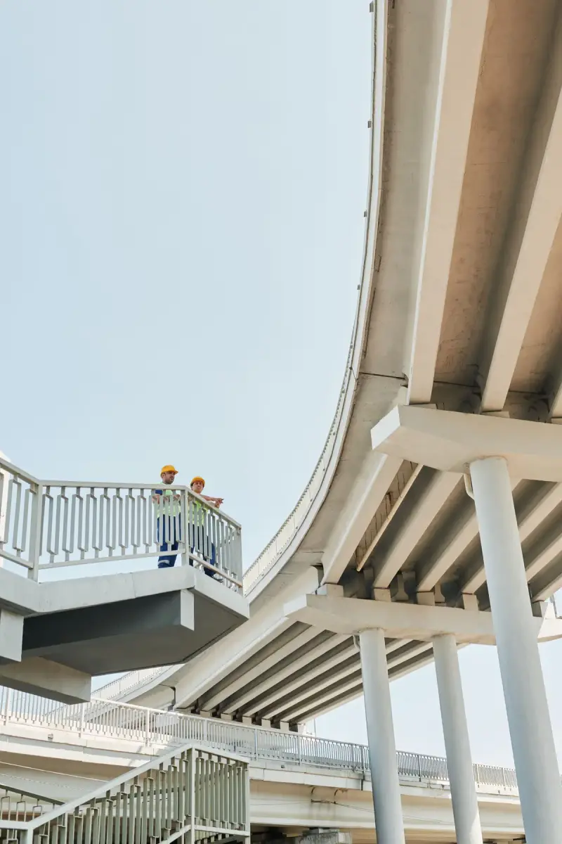 Two engineers in safety gear looking out at a modern overpass structure