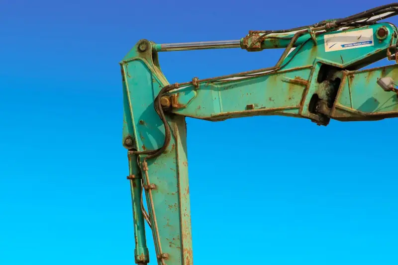 Turquoise excavator boom and hydraulic cylinders against a clear blue sky