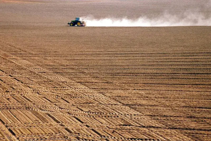 Tractor trailing a dust cloud across a vast tilled field with neat rows