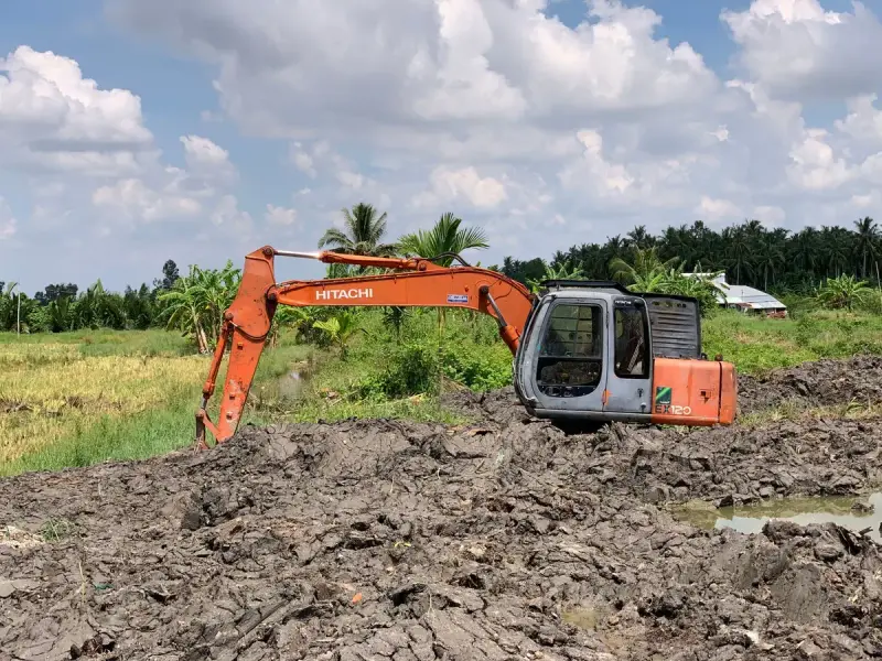 Orange excavator standing in a rural field under a bright blue sky