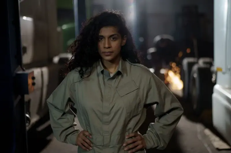 Female mechanic in a gray jumpsuit standing among workshop machinery