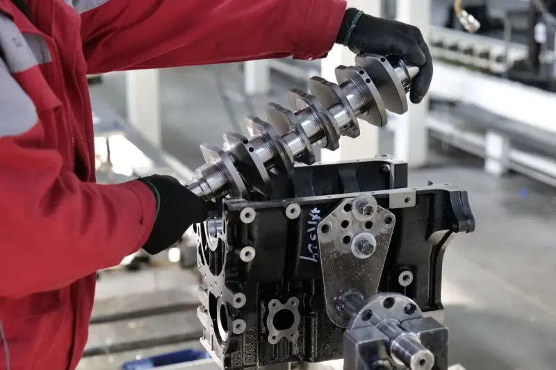 Technician in red overalls lowering a crankshaft into an engine block