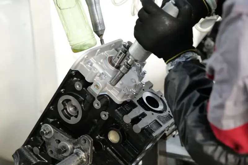 Gloved hands using a power tool to fasten parts on an engine cylinder head