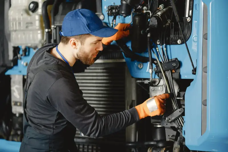 Mechanic in a blue cap and gloves working on the engine of a blue truck