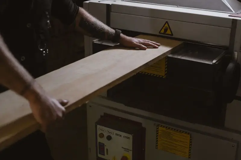 Woodworker feeding a board through a thickness planer in a joinery shop