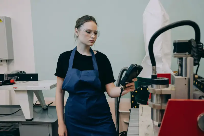 Woman in safety goggles and apron operating a machine in a workshop
