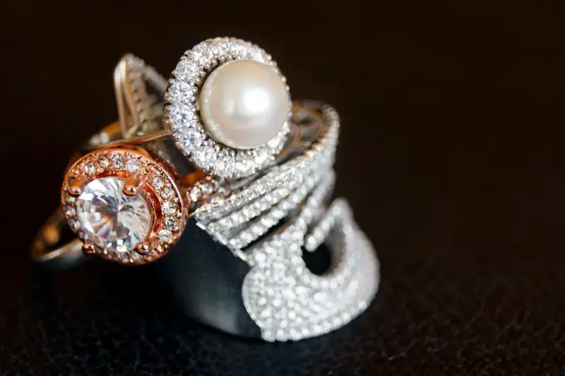 Stacked diamond halo, pearl and pavé fashion rings on a black background