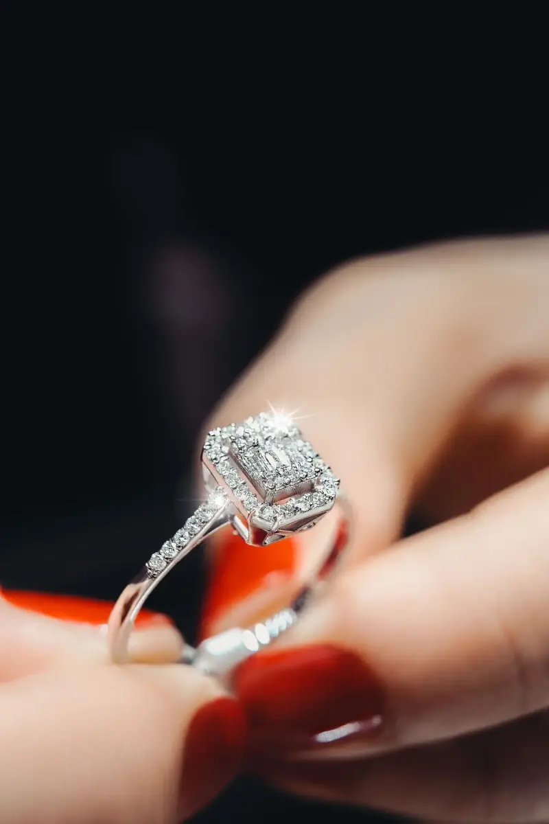 Hand with red nails holding a cushion-cut diamond halo engagement ring