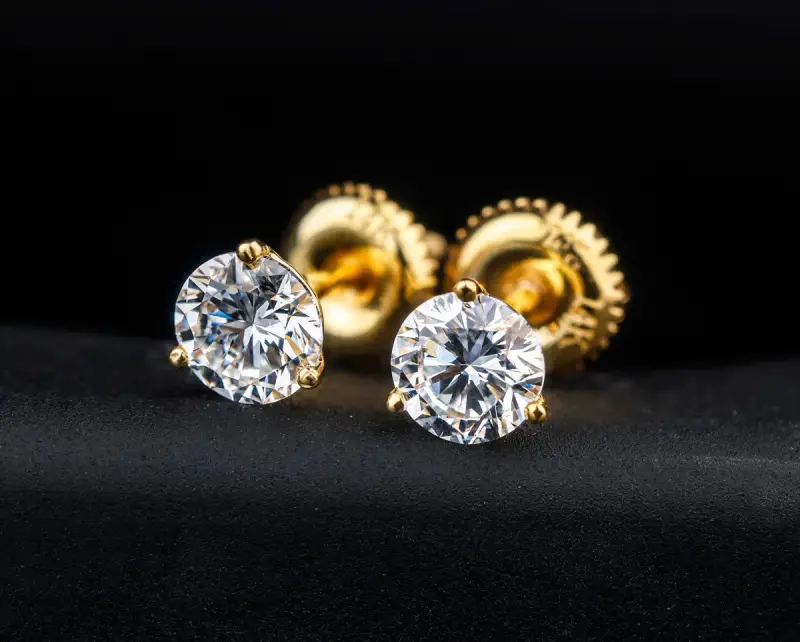Pair of round diamond stud earrings in yellow gold on a black surface
