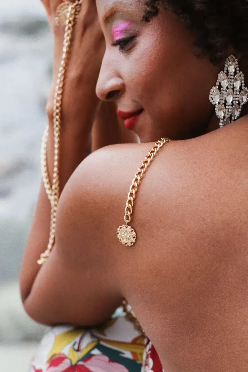 Close-up of an adult woman wearing sparkling drop earrings and holding a gold-toned chain across her shoulder.