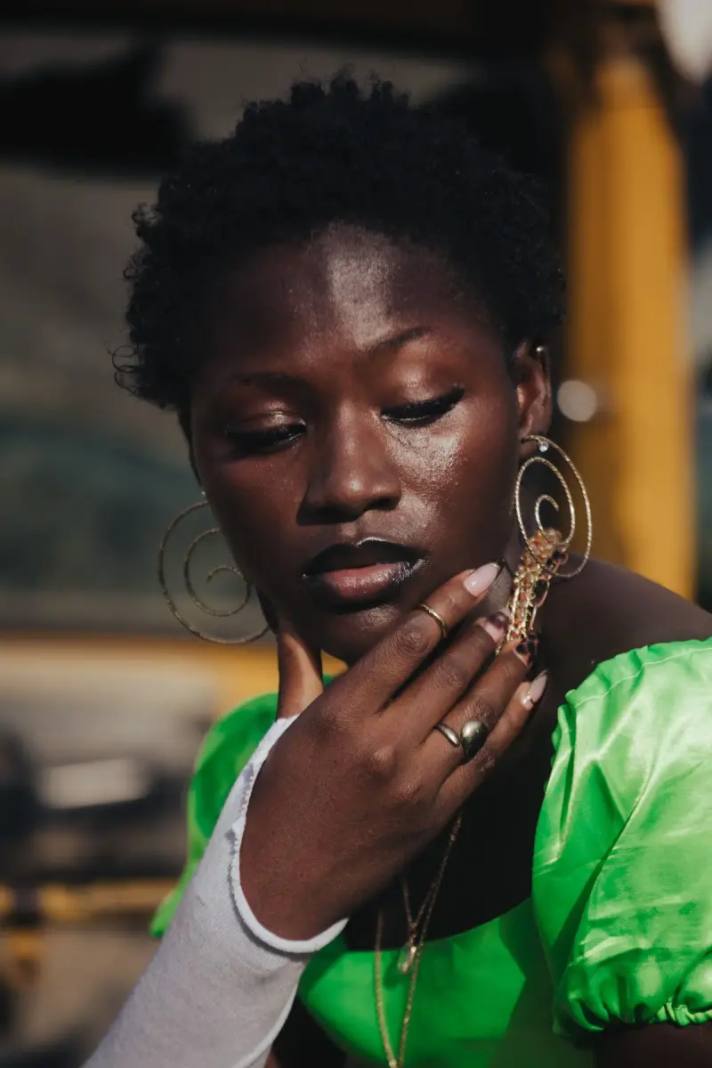 Woman in a bright green dress wearing oversized gold hoop earrings and rings in warm sun