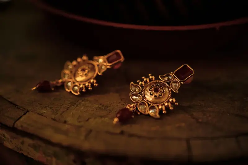 Gold earrings set with colored gemstones laid on a rustic wooden surface