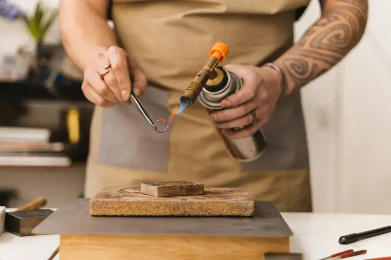 Jeweler using a small torch to work on a gold ring at a workbench
