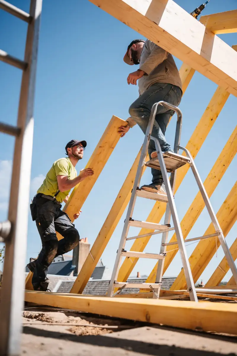 Two workers building a wooden roof structure on a sunny day