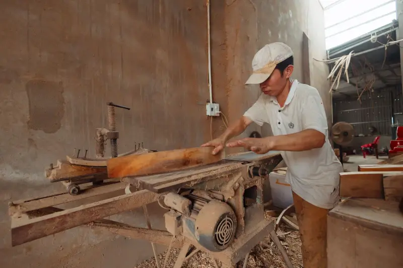 Carpenter cutting wood on a saw in a dusty workshop