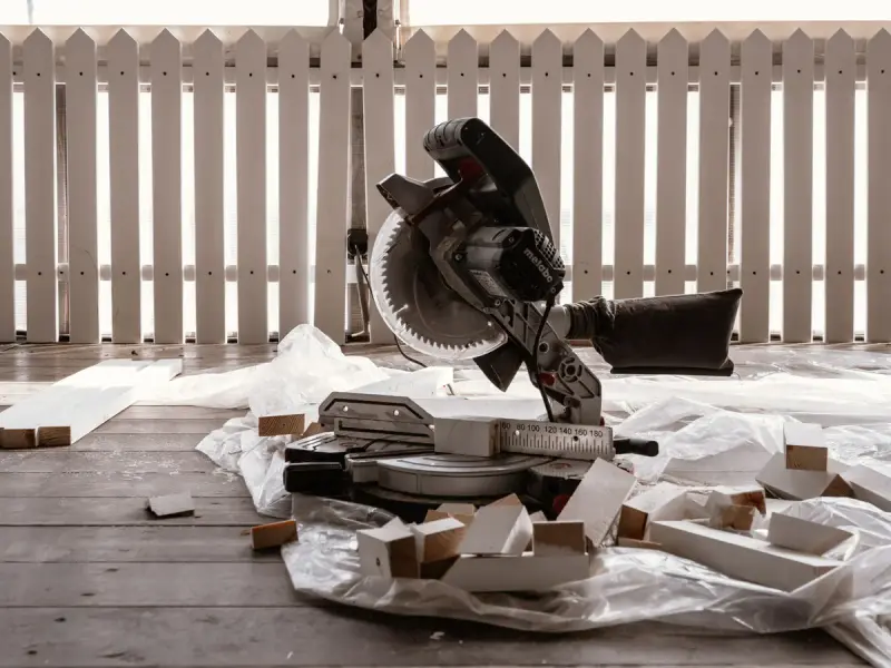 Miter saw on a wooden terrace with offcuts on a drop cloth beside a white fence
