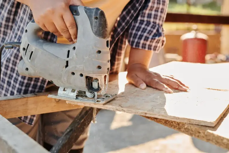 Carpenter cutting plywood with a jigsaw at a construction site