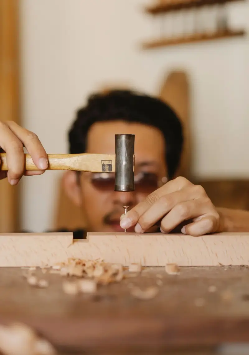 Carpenter hammering a nail into a wooden beam in a workshop