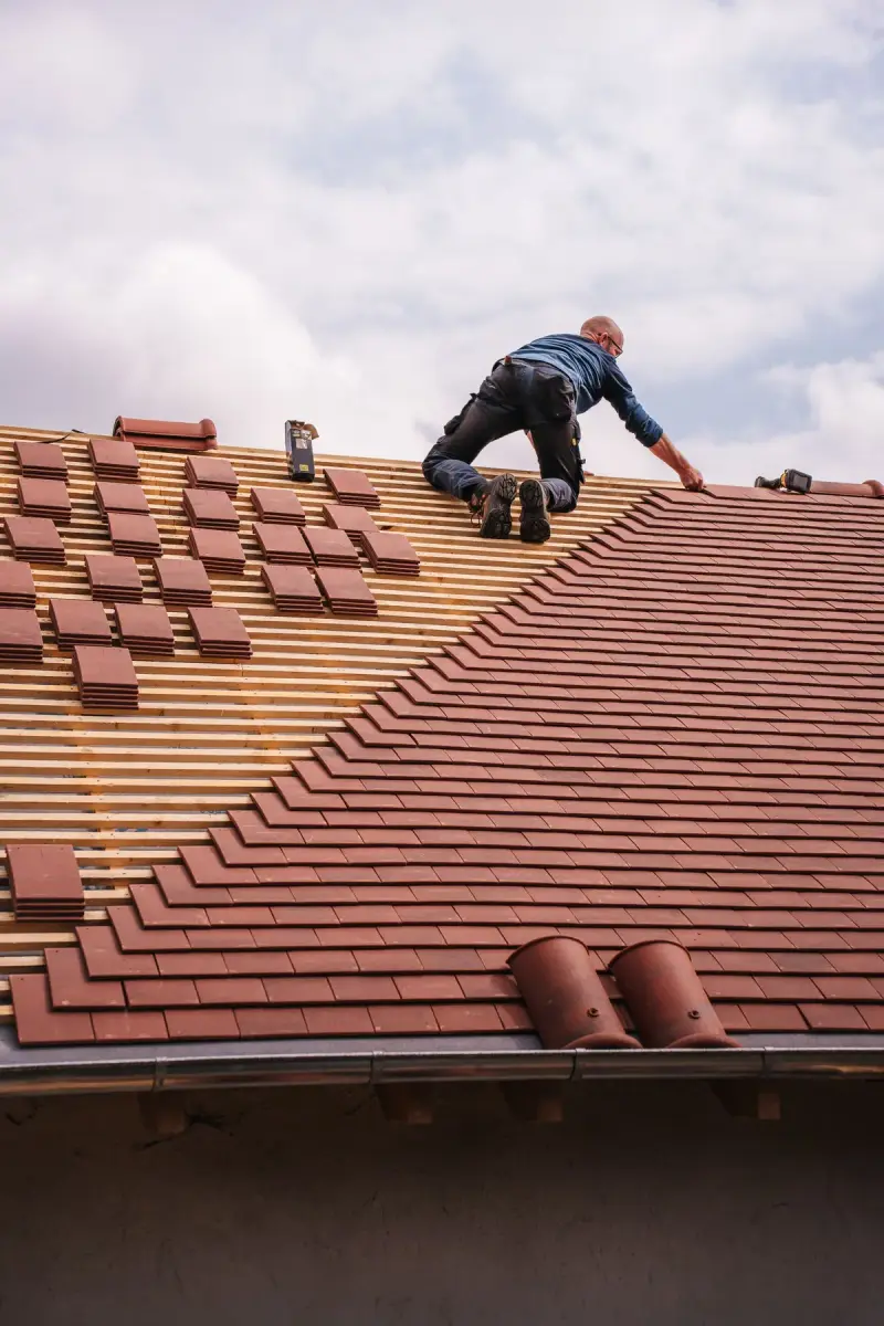 Roofer laying red clay tiles on a new pitched roof