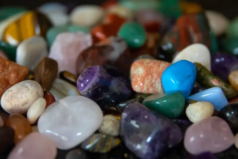 A heap of polished tumbled gemstones in purple, blue, green and amber tones
