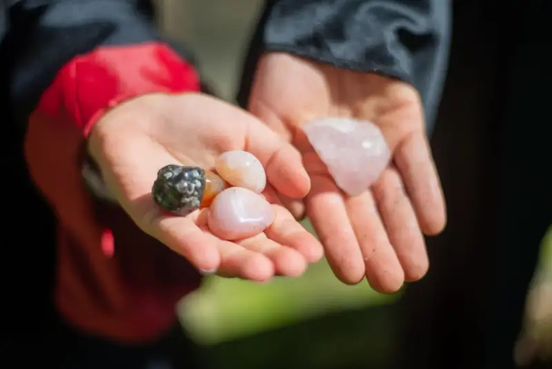 Two cupped hands holding polished pink and grey gemstones outdoors