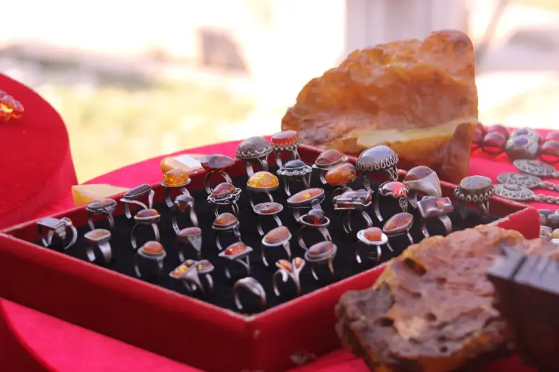 Tray of amber and gemstone silver rings on red velvet beside raw amber
