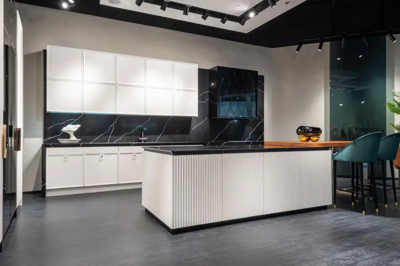 Showroom kitchen with white cabinets, a ribbed island and black stone counters under track lights