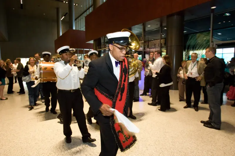 A New Orleans brass band parades through a convention center lobby past badge-wearing KBIS attendees