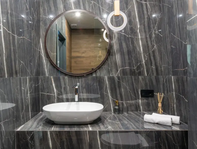 Vessel sink on a dark marble vanity with a round mirror and ring light
