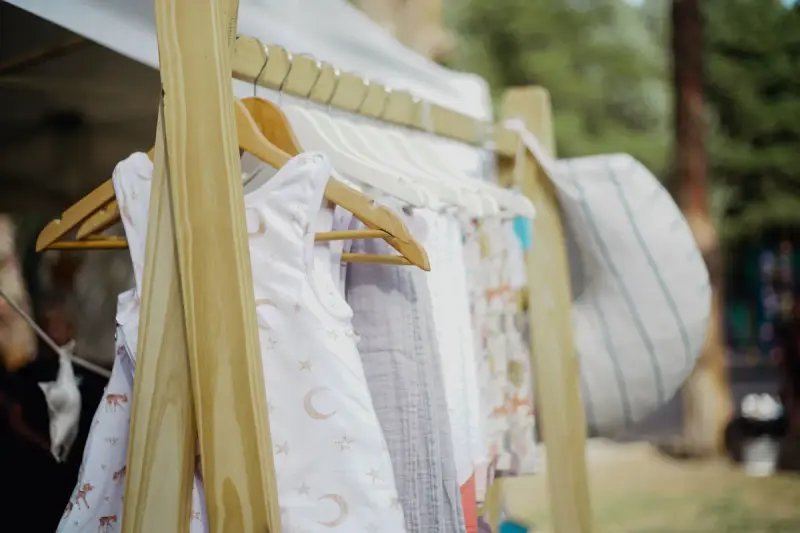 Baby dresses and rompers in soft prints on wooden hangers at an outdoor stall
