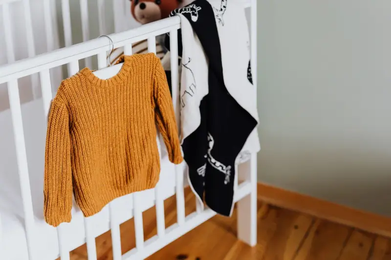 Mustard knit baby sweater and patterned blanket hanging on a white wooden crib