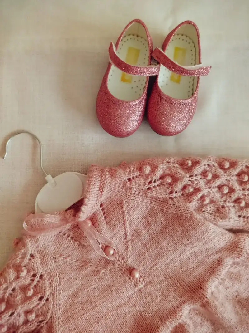 Pink knit baby cardigan on a hanger with glittery pink Mary Jane shoes