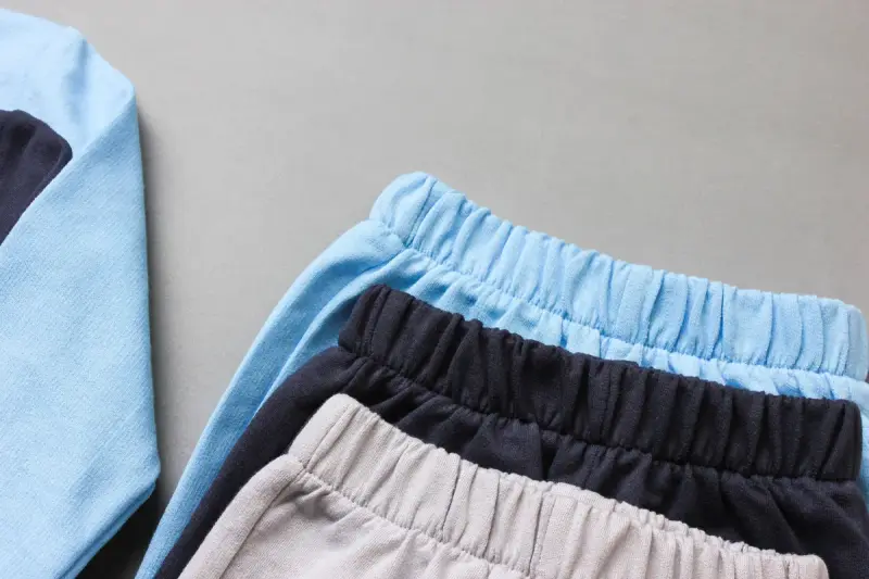 Stack of baby joggers in sky blue, navy and soft gray on a gray surface
