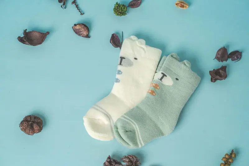 Two pairs of baby socks with bear faces on a blue background with dried leaves